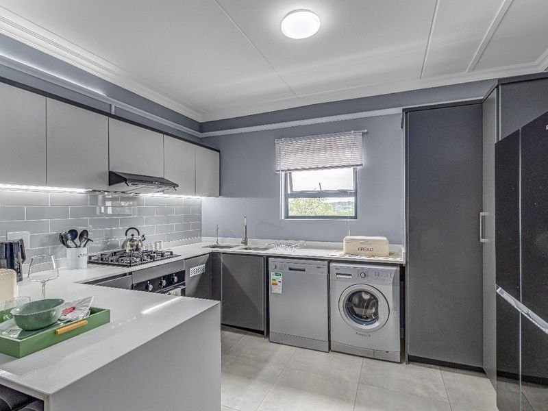 Modern kitchen featuring sleek grey cabinetry, quartz countertops, subway tile backsplash, gas hob, extractor fan, and integrated space for laundry and dishwashing appliances.