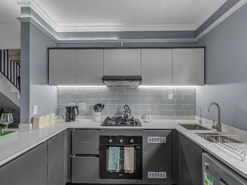 Modern kitchen featuring sleek grey cabinetry, quartz countertops, subway tile backsplash, integrated gas hob, oven, and extractor fan with elegant crown molding.