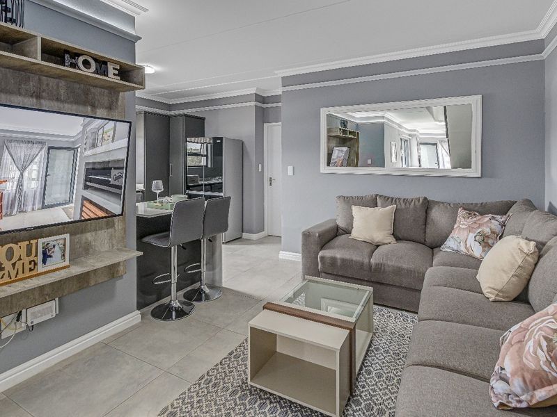 Modern open-plan living area featuring tiled floors, crown molding, and a functional kitchen with a breakfast bar, creating a cohesive and well-maintained space.