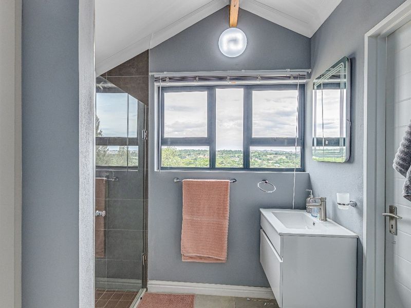 Modern bathroom featuring a floating vanity, glass-enclosed shower, vaulted ceiling, and a window with scenic views.