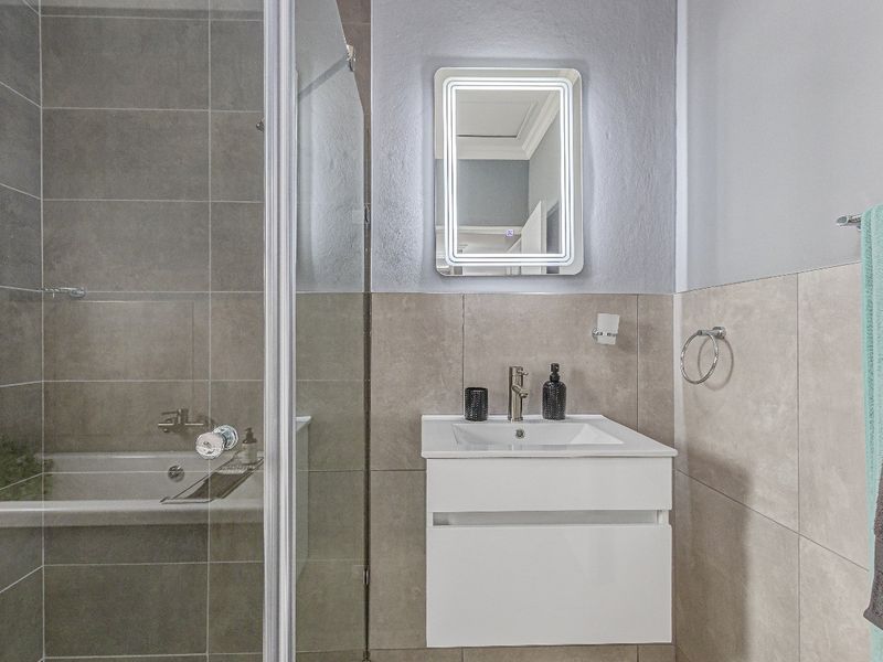 Modern bathroom featuring a wall-mounted vanity with integrated basin, LED backlit mirror, and a glass-enclosed shower and bathtub combination with neutral tiling.