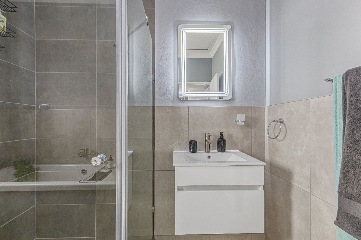Modern bathroom featuring a wall-mounted vanity with integrated basin, LED backlit mirror, and a glass-enclosed shower and bathtub combination with neutral tiling.