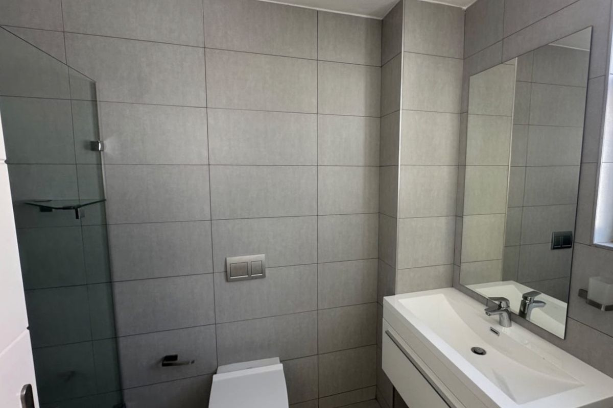 Modern bathroom featuring a floating vanity with integrated basin, wall-mounted toilet, and large-format grey ceramic tiling throughout.