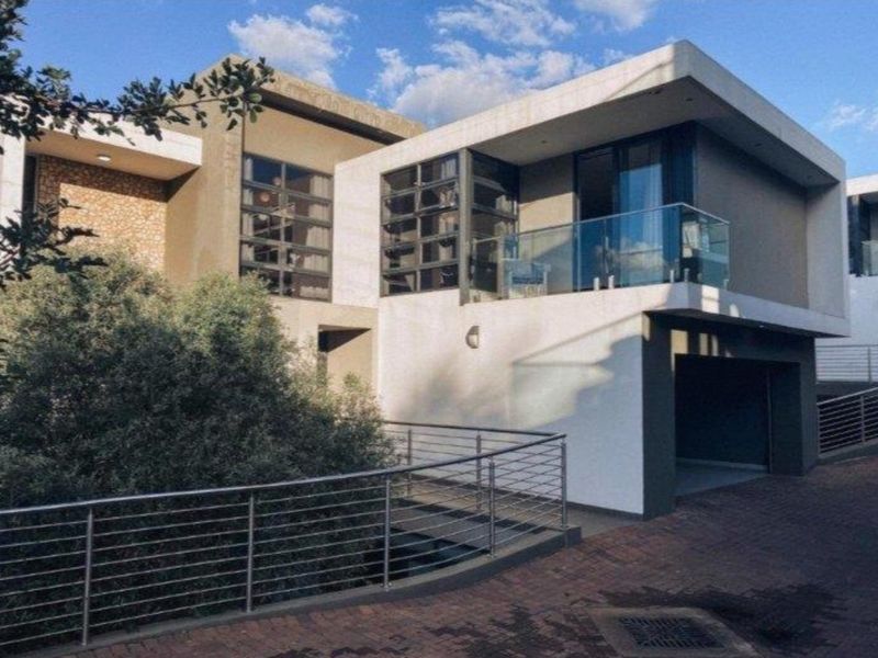 Modern two-story residential facade featuring stone cladding, a glass balcony, and a paved driveway leading to a garage.