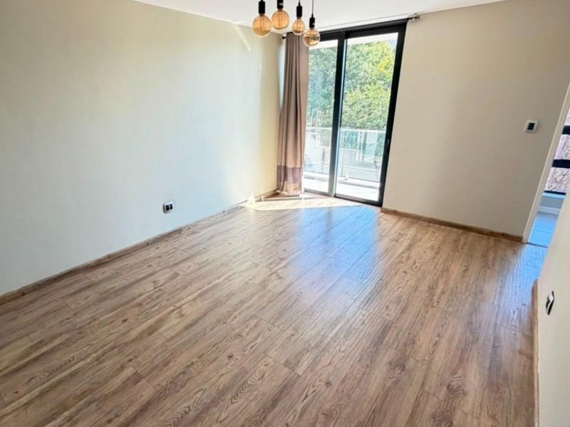 A bright, empty bedroom featuring modern laminate flooring, neutral walls, and a sliding glass door providing access to an outdoor balcony.