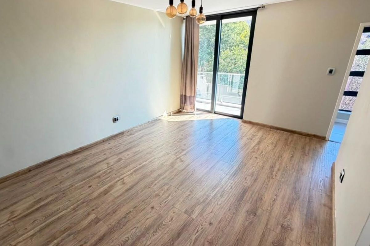 A bright, empty bedroom featuring modern laminate flooring, neutral walls, and a sliding glass door providing access to an outdoor balcony.