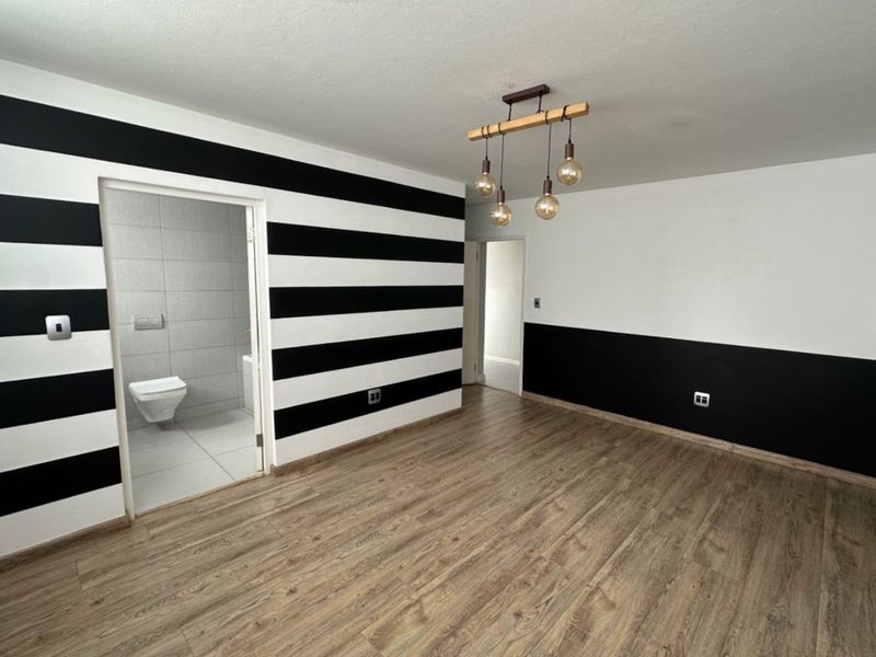 An empty living room featuring wood-look laminate flooring and a modern pendant light, with an adjacent bathroom visible through the doorway.