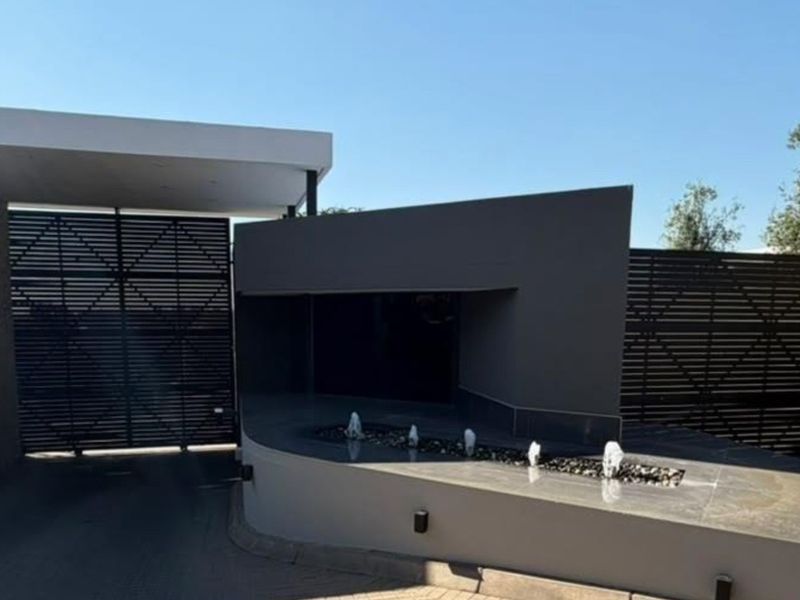 Modern gated entrance featuring stone cladding, a sleek water feature, and contemporary architectural design elements.