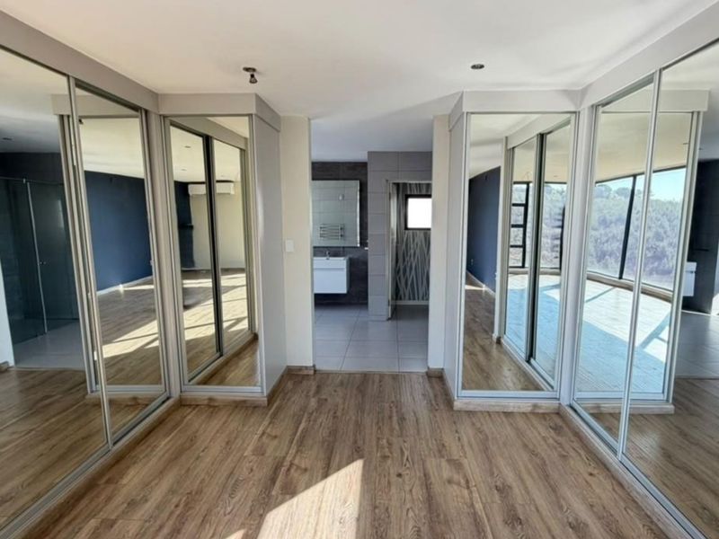 Spacious bedroom featuring extensive built-in mirrored wardrobes, laminate flooring, and direct access to an en-suite bathroom.