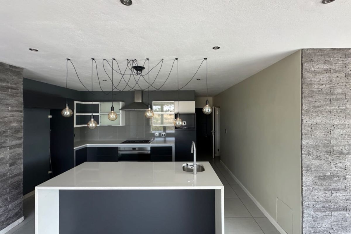 Modern kitchen featuring a central island with stone countertop, built-in oven, gas hob, extractor fan, and stylish pendant lighting in an open-plan layout.