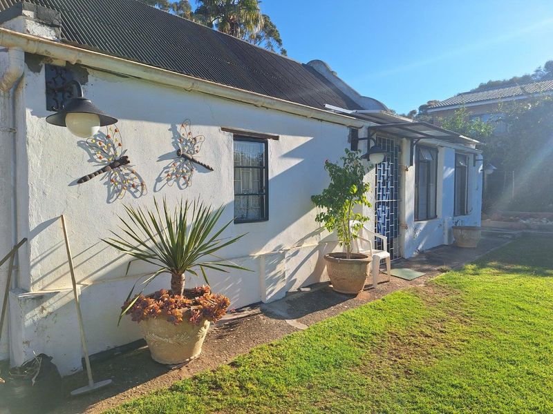 Rear exterior view of a cottage-style home featuring a corrugated metal roof, security gate, and a paved walkway adjacent to a garden area.