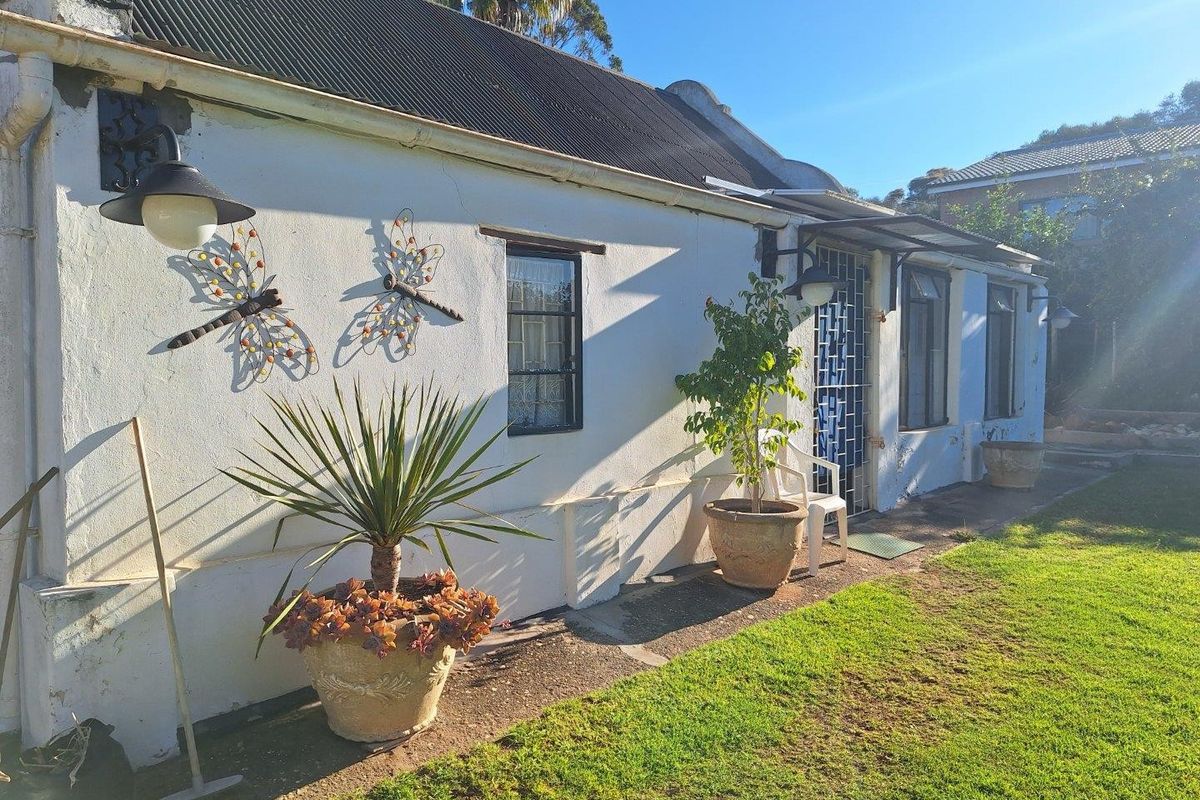 Rear exterior view of a cottage-style home featuring a corrugated metal roof, security gate, and a paved walkway adjacent to a garden area.