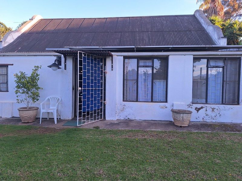 Rear exterior view of a cottage-style house featuring a corrugated metal roof, security gates, and metal-framed windows with visible exterior wall wear.