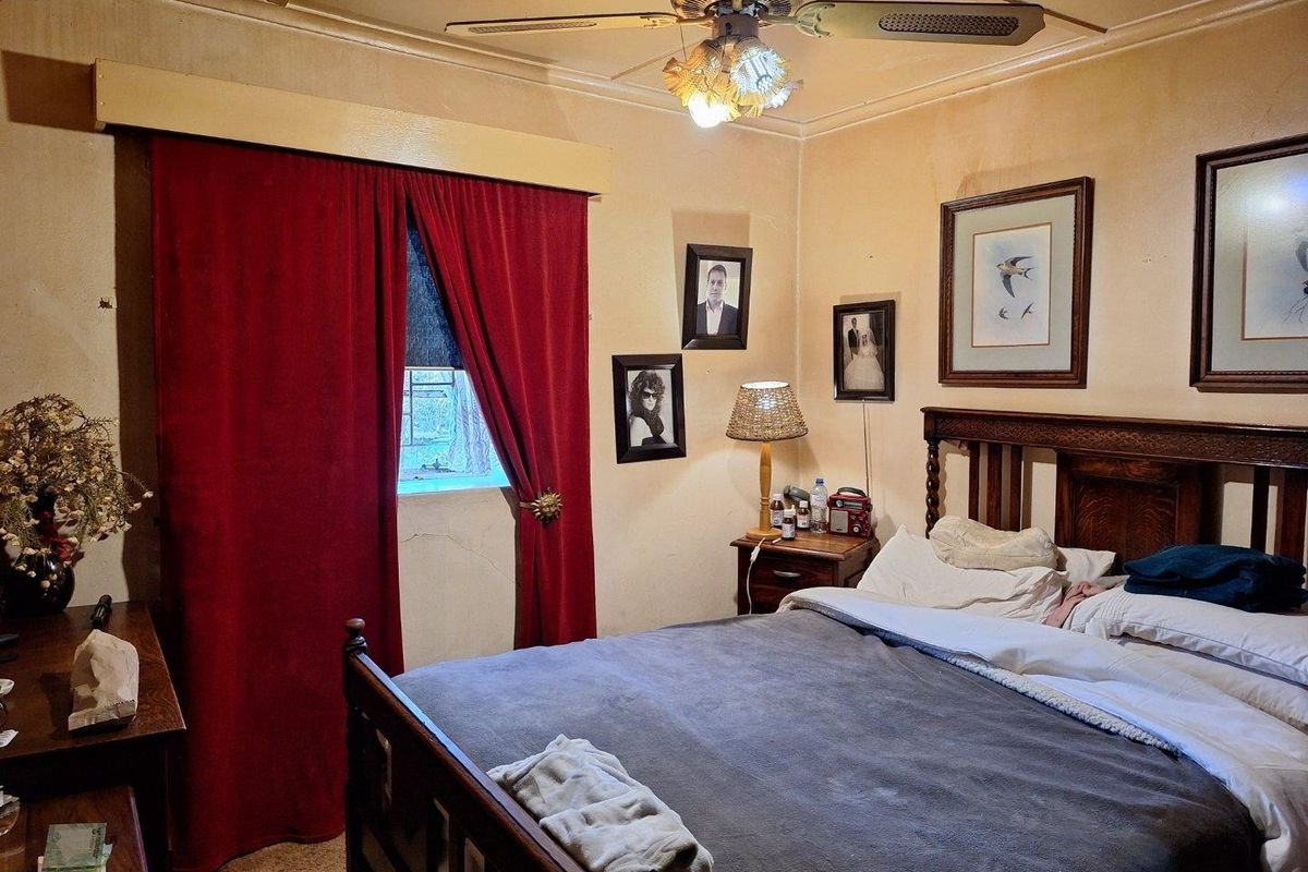 A bedroom featuring a ceiling fan and coved ceiling, showing signs of wear including cracked plaster and stained wall finishes.