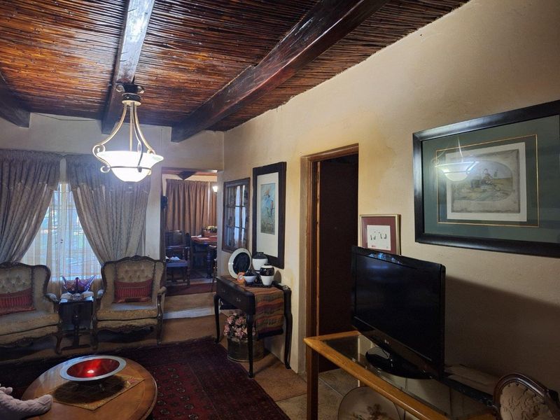 A living room featuring a rustic exposed timber beam and reed ceiling, with access to adjacent rooms and traditional architectural finishes.