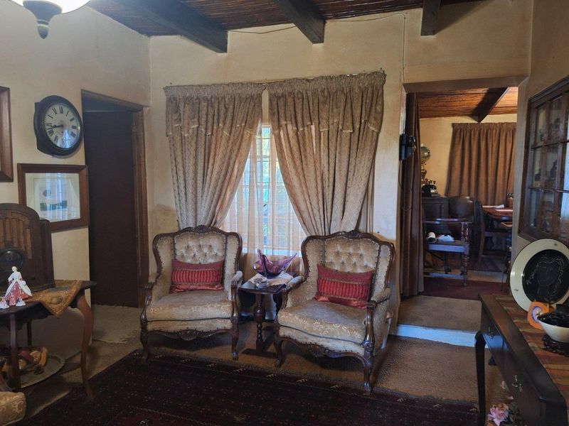 A traditional living room featuring exposed timber ceiling beams and a window with security bars, showcasing a dated aesthetic.