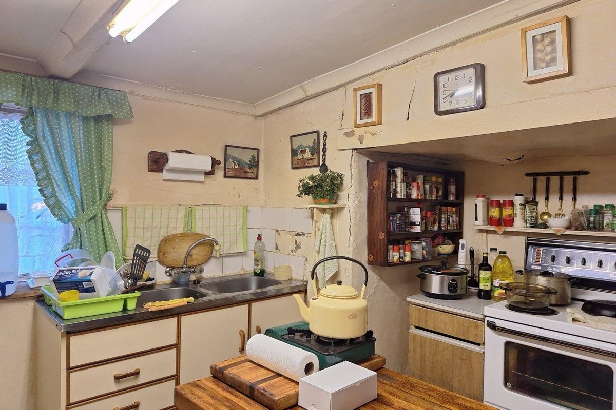 A dated kitchen featuring a double bowl sink, built-in oven, and cooktop, requiring significant cosmetic updates and wall repairs to modernize the space.