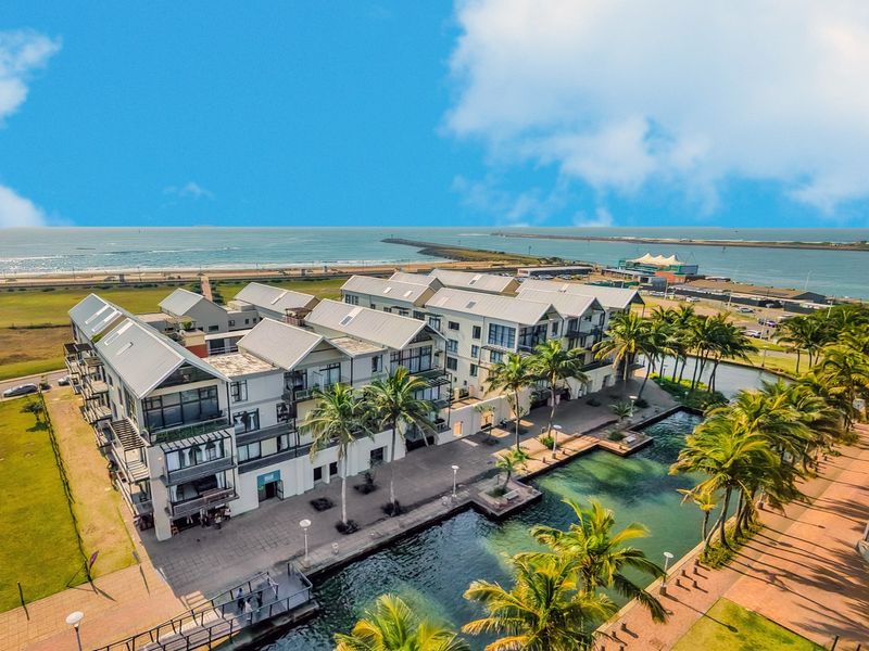 Aerial view of a modern apartment complex featuring pitched roofs, private balconies, and landscaped waterfront walkways overlooking the ocean.