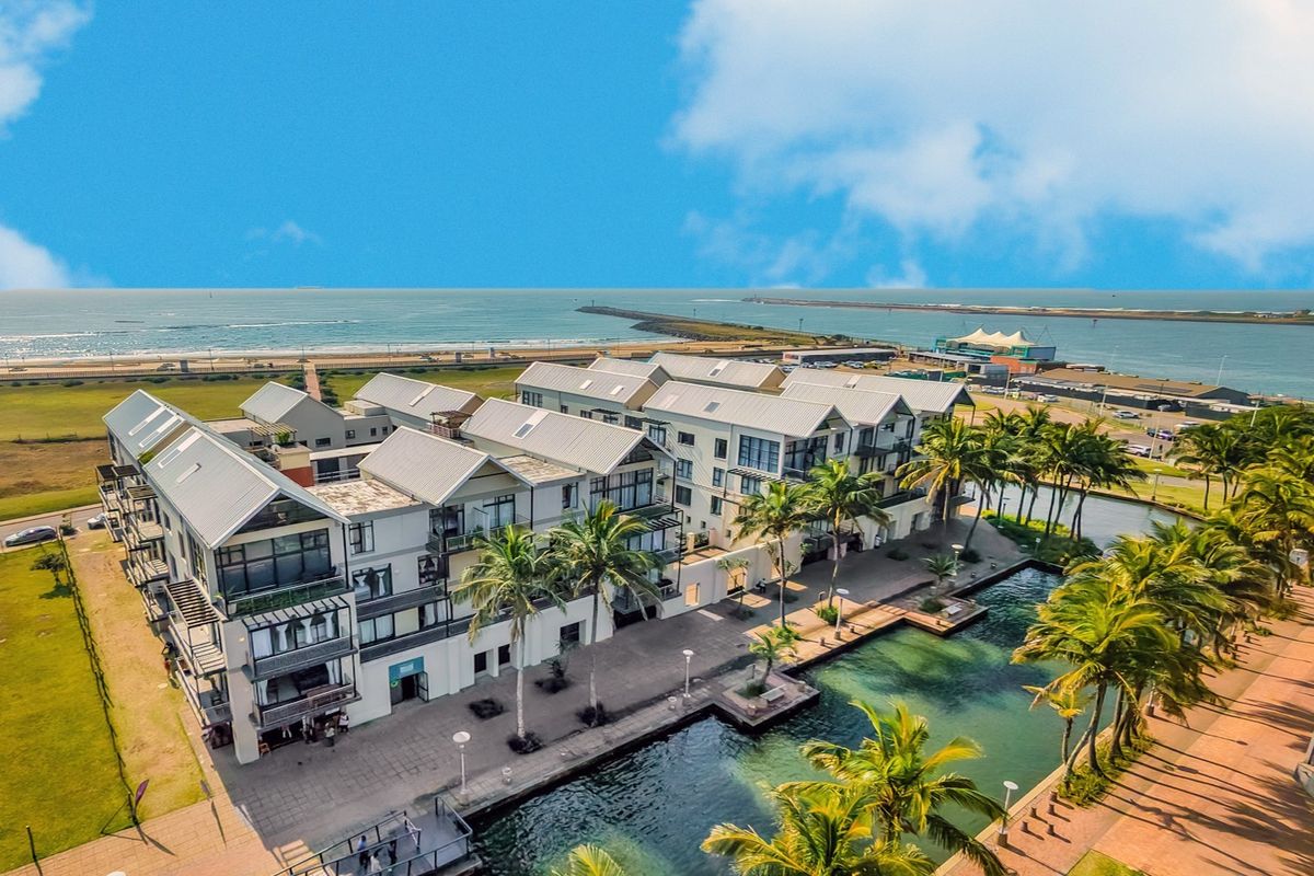 Aerial view of a modern apartment complex featuring pitched roofs, private balconies, and landscaped waterfront walkways overlooking the ocean.
