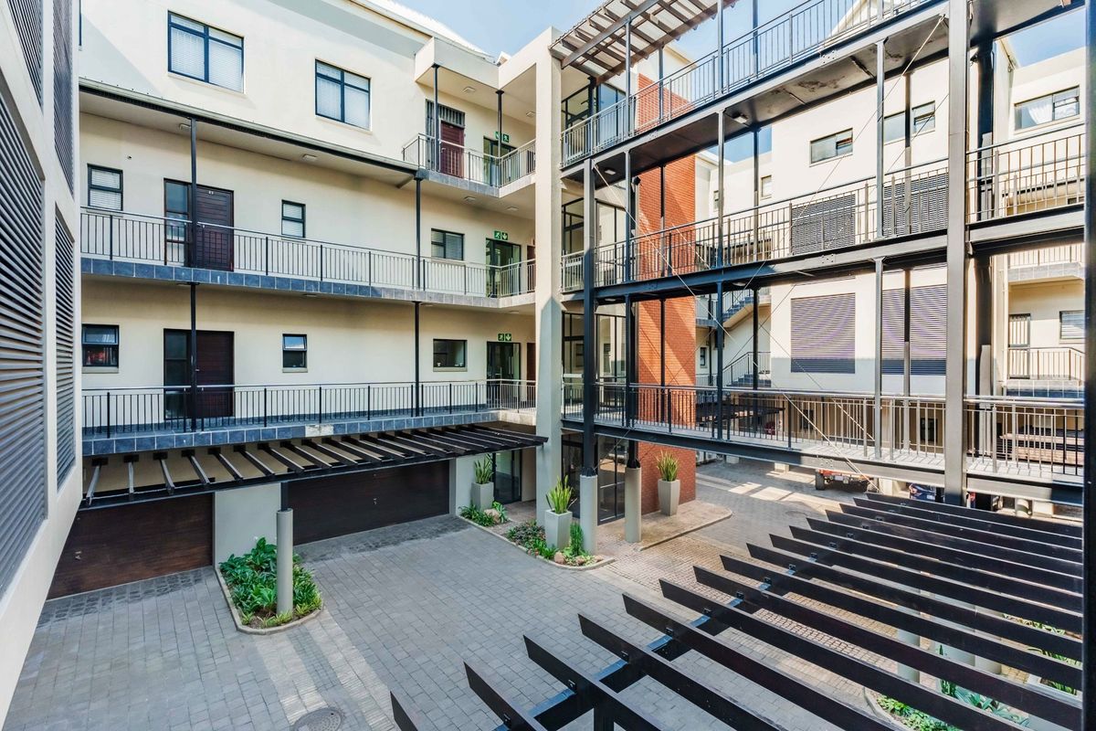 A modern apartment complex courtyard featuring multi-level metal walkways, paved ground level, and architectural timber pergolas.
