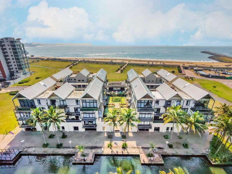 Aerial view of a modern apartment complex featuring pitched roofs, private balconies, and a central landscaped courtyard situated near the coastline.