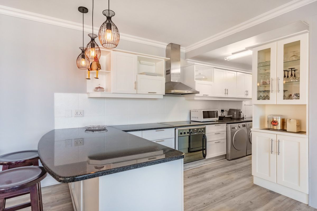 Modern kitchen featuring white cabinetry, granite countertops, integrated appliances, and a breakfast bar, complemented by stylish pendant lighting and light wood-look laminate flooring.