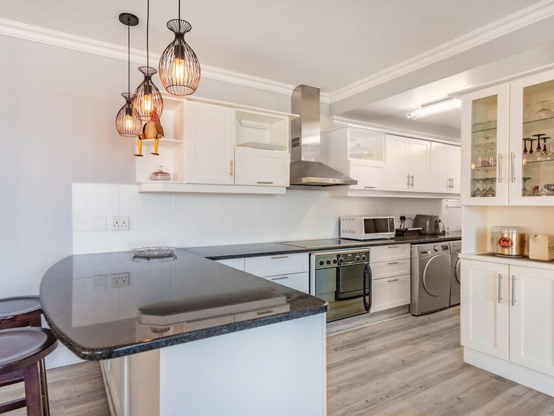Modern kitchen featuring white cabinetry, granite countertops, integrated appliances, and a breakfast bar, complemented by stylish pendant lighting and light wood-look laminate flooring.