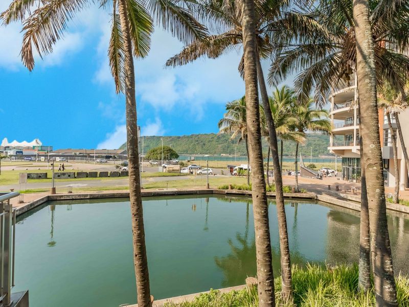 A scenic view overlooking a tranquil water feature and landscaped grounds with palm trees, captured from an elevated balcony.