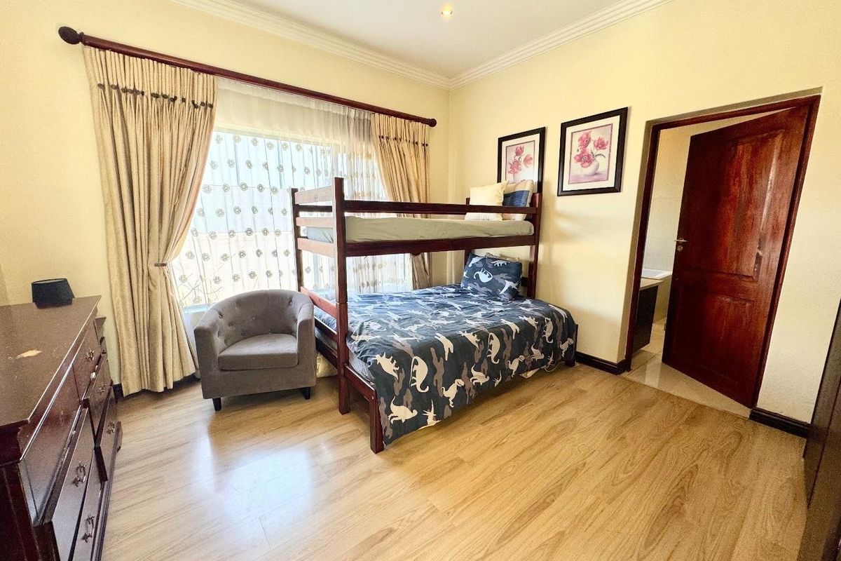A well-maintained bedroom featuring laminate flooring, coved cornicing, and recessed lighting, with an adjoining doorway leading to an en-suite bathroom.