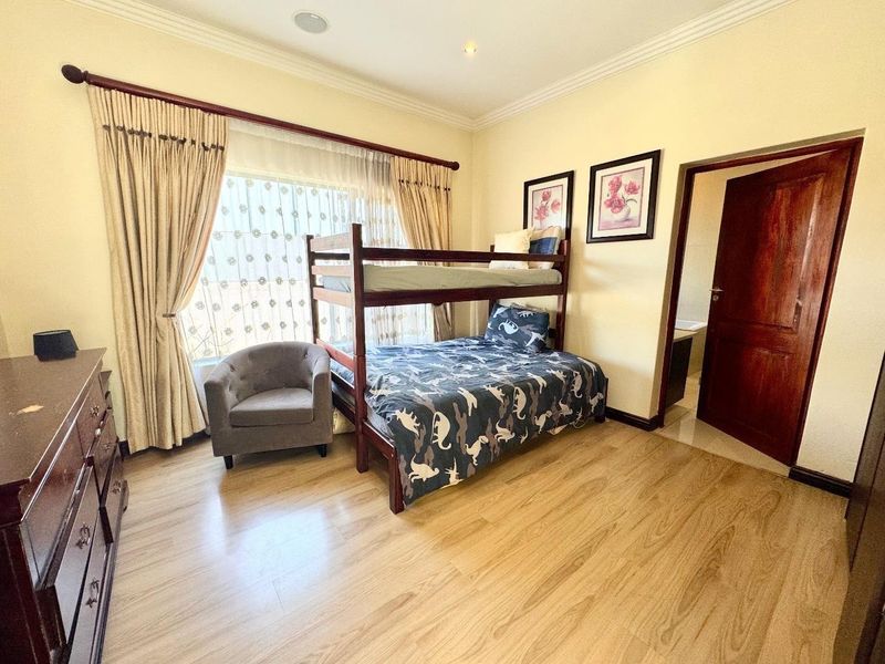 A well-maintained bedroom featuring laminate flooring, coved cornicing, and recessed lighting, with an adjoining doorway leading to an en-suite bathroom.