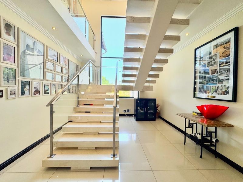 Spacious double-volume entrance hall featuring a modern floating staircase with glass balustrades and polished porcelain floor tiles.