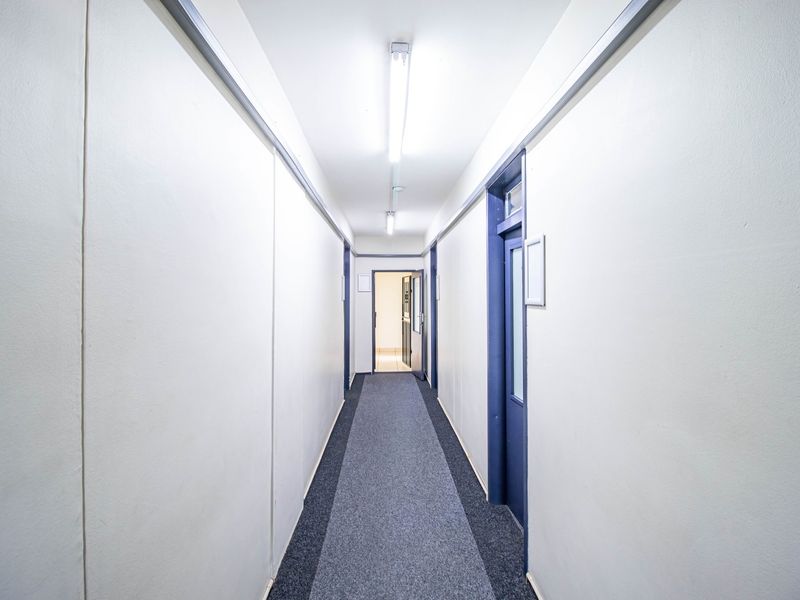 A clean, functional commercial hallway featuring neutral walls, carpeted flooring, and multiple access doors, providing efficient circulation between office or utility spaces.