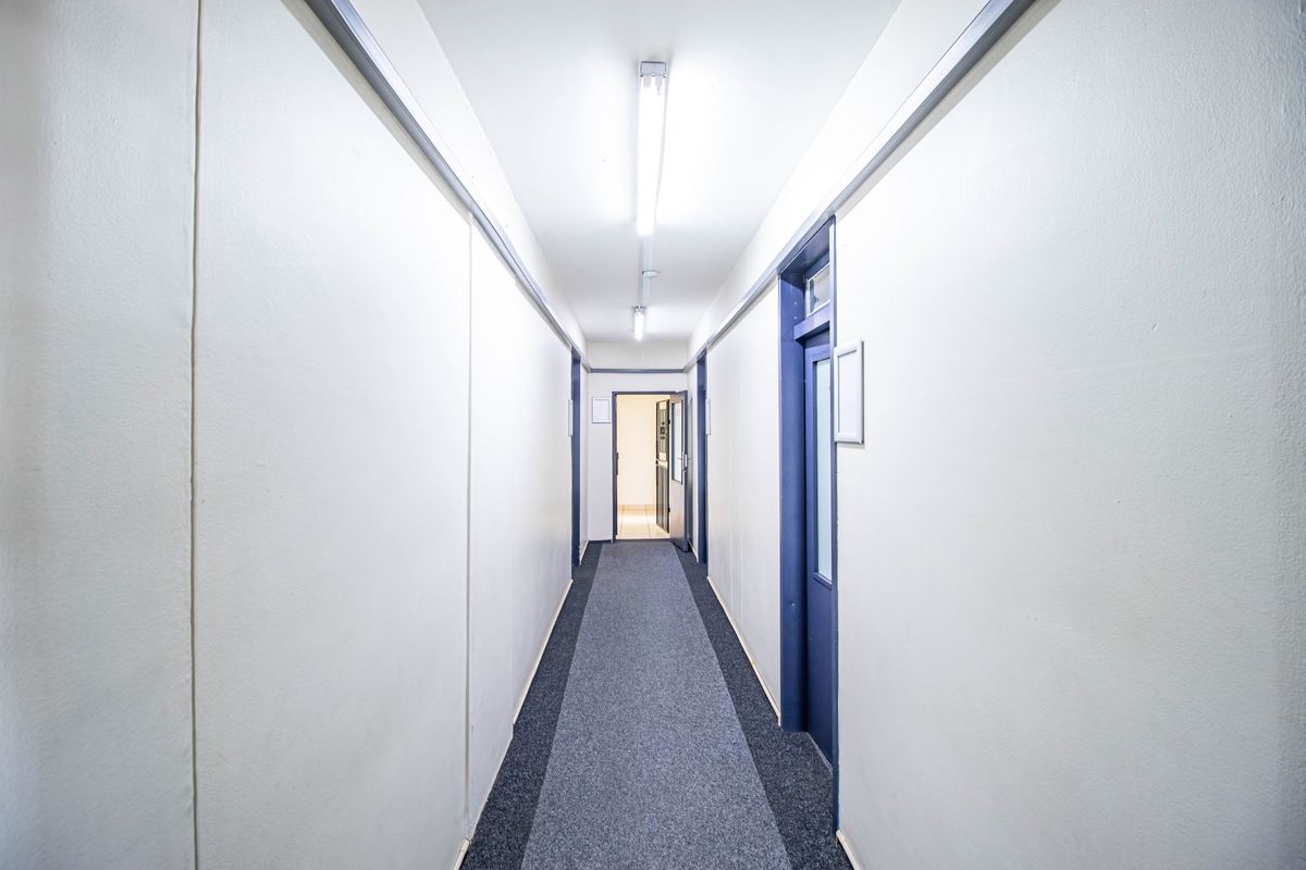 A clean, functional commercial hallway featuring neutral walls, carpeted flooring, and multiple access doors, providing efficient circulation between office or utility spaces.