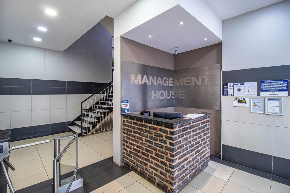 Commercial building entrance featuring a brick-faced reception desk, metal signage, secure turnstile access, and a staircase leading to upper levels.