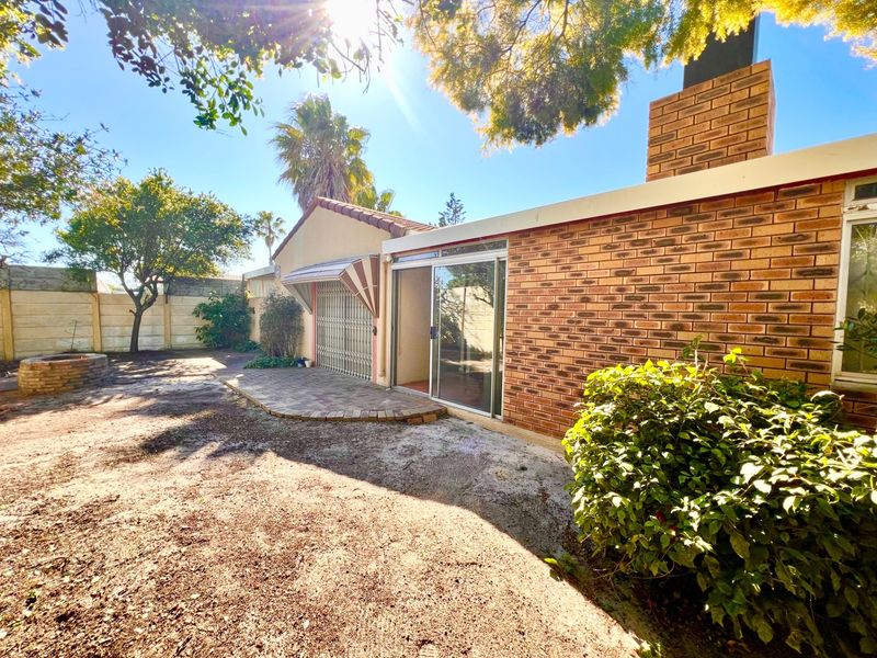 Rear exterior view of the property featuring a brick facade, chimney, sliding glass door access, and a paved patio area leading to the garden.