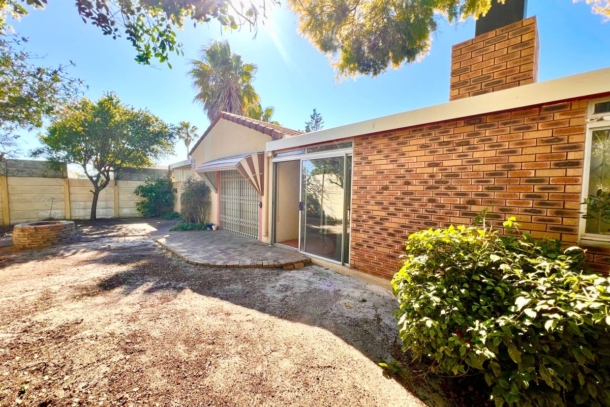 Rear exterior view of the property featuring a brick facade, chimney, sliding glass door access, and a paved patio area leading to the garden.