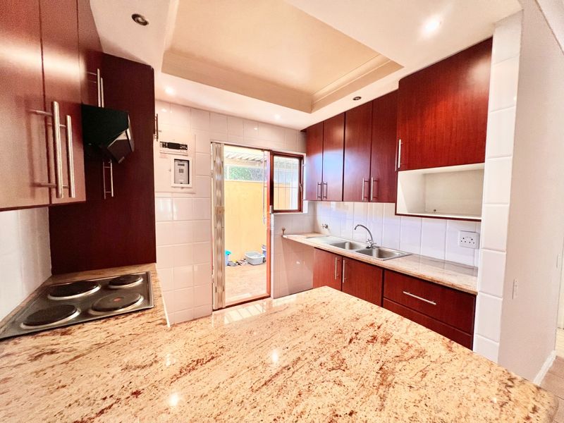 A functional kitchen featuring dark wood cabinetry, granite countertops, an electric hob, and a tiled backsplash with direct access to an outdoor area.