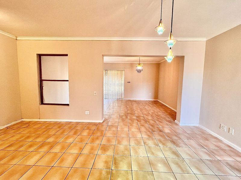 Spacious open-plan living area featuring neutral walls, ceramic tiled flooring, and natural light through a sliding glass door with security gate.