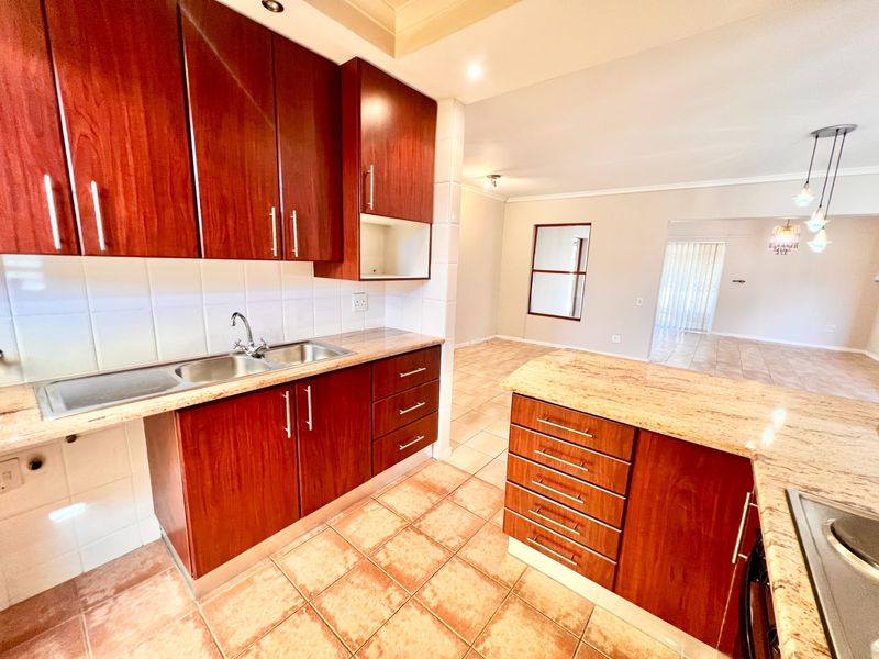Open-plan kitchen featuring warm-toned wooden cabinetry, granite countertops, and tiled flooring, flowing into an adjacent living area.
