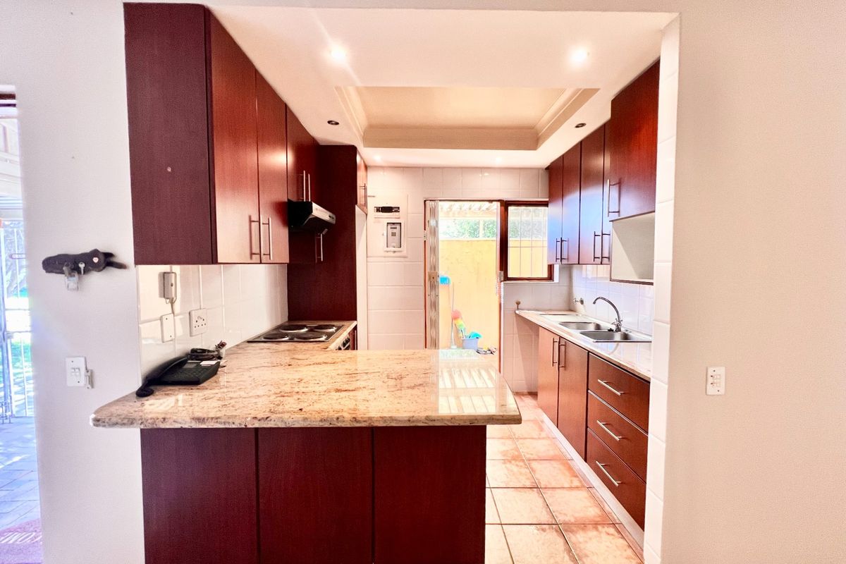 A functional kitchen featuring dark wood cabinetry, granite countertops, an electric hob with extractor, and a double basin sink with tiled flooring.
