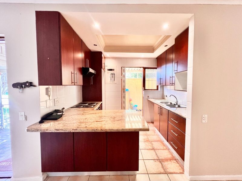 A functional kitchen featuring dark wood cabinetry, granite countertops, an electric hob with extractor, and a double basin sink with tiled flooring.