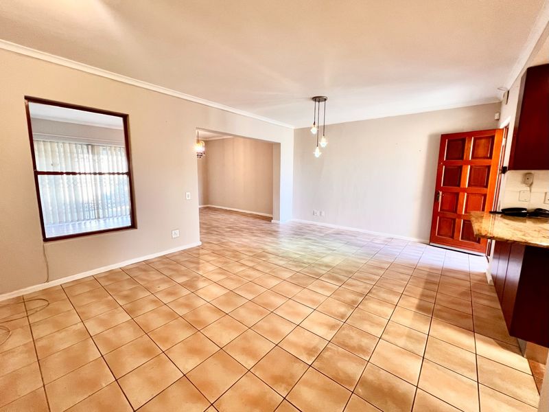 Spacious open-plan living and kitchen area featuring ceramic tile flooring, neutral walls, and a classic wooden door, offering a versatile layout for modern living.