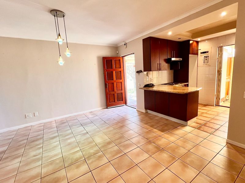 Open-plan living and kitchen area featuring tiled flooring, dark wood cabinetry, granite countertops, and a direct entrance to the exterior.