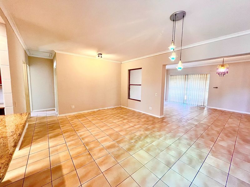 Spacious open-plan living area featuring neutral tiled flooring, modern pendant lighting, and a sliding glass door leading to the exterior.