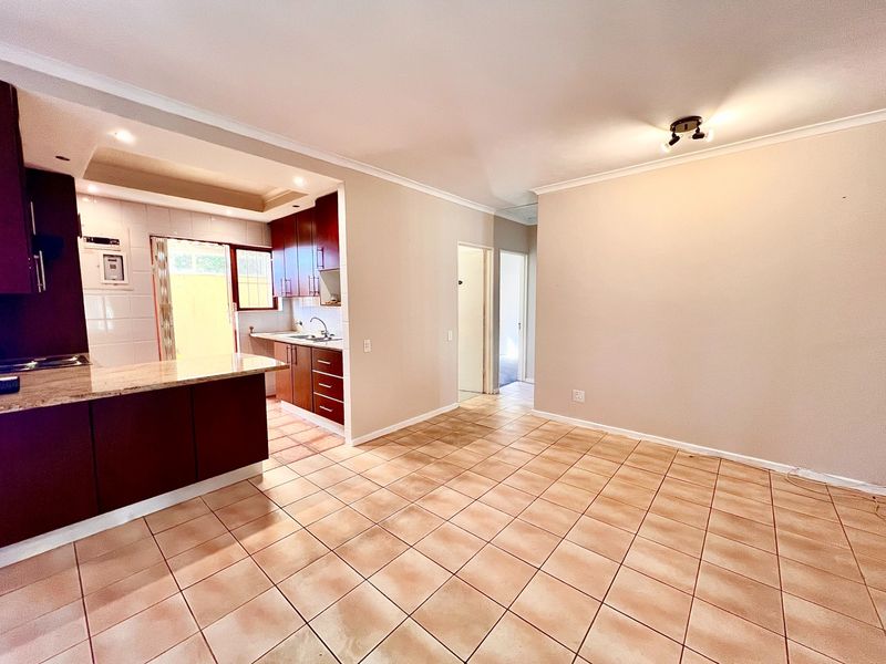 An open-plan living and kitchen area featuring tiled floors, dark wood cabinetry, granite countertops, and neutral wall finishes in a vacant, well-lit space.