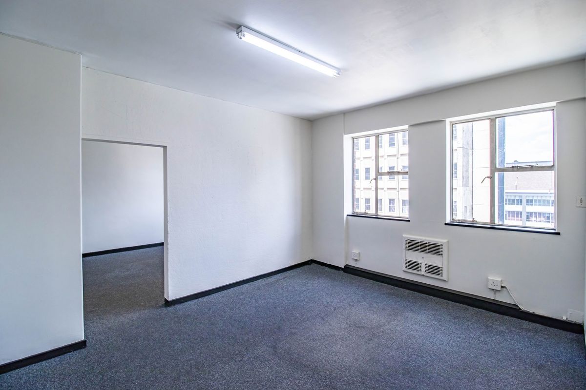 A vacant, open-plan office space featuring grey carpeting, built-in air conditioning, and natural light from large windows.