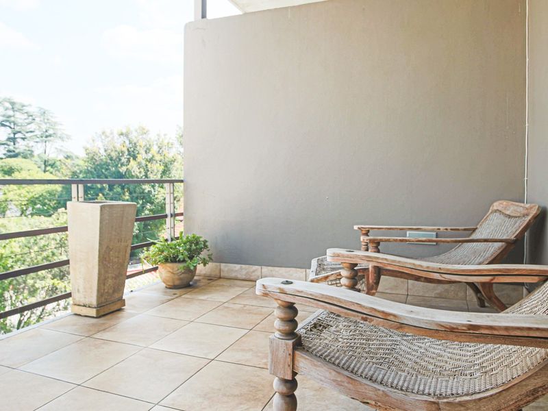A covered balcony featuring tiled flooring and a metal railing, offering an open outdoor space with views of the surrounding greenery.