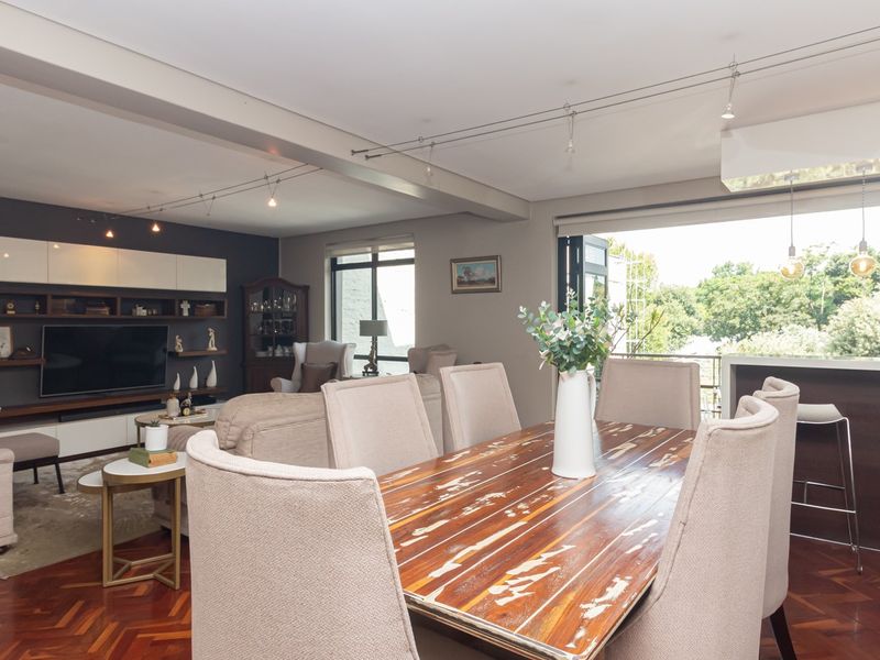 Spacious open-plan living and dining area featuring rich parquet flooring, modern track lighting, and seamless access to an outdoor balcony through bi-fold doors.