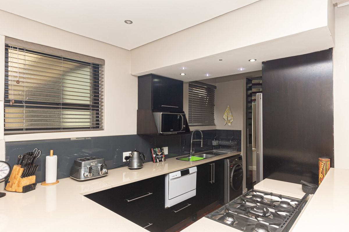 Modern kitchen featuring sleek black cabinetry, stone countertops, a gas hob, integrated microwave, and high-quality finishes throughout.