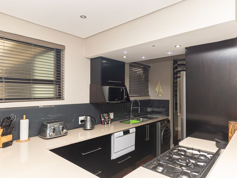 Modern kitchen featuring sleek black cabinetry, stone countertops, a gas hob, integrated microwave, and high-quality finishes throughout.